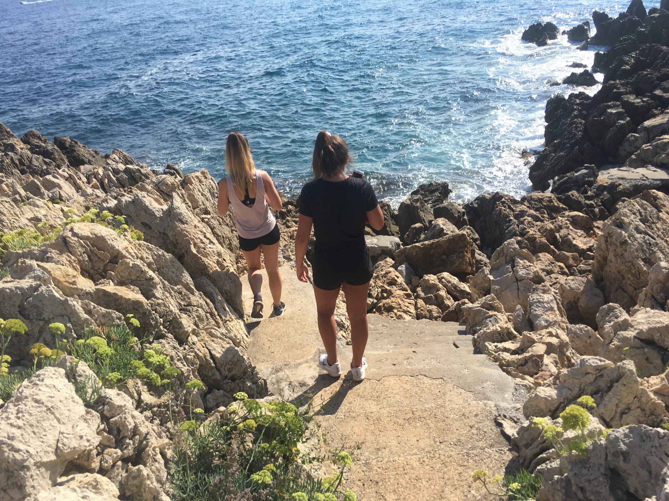 two women walking down on a cliff overlooking the ocean